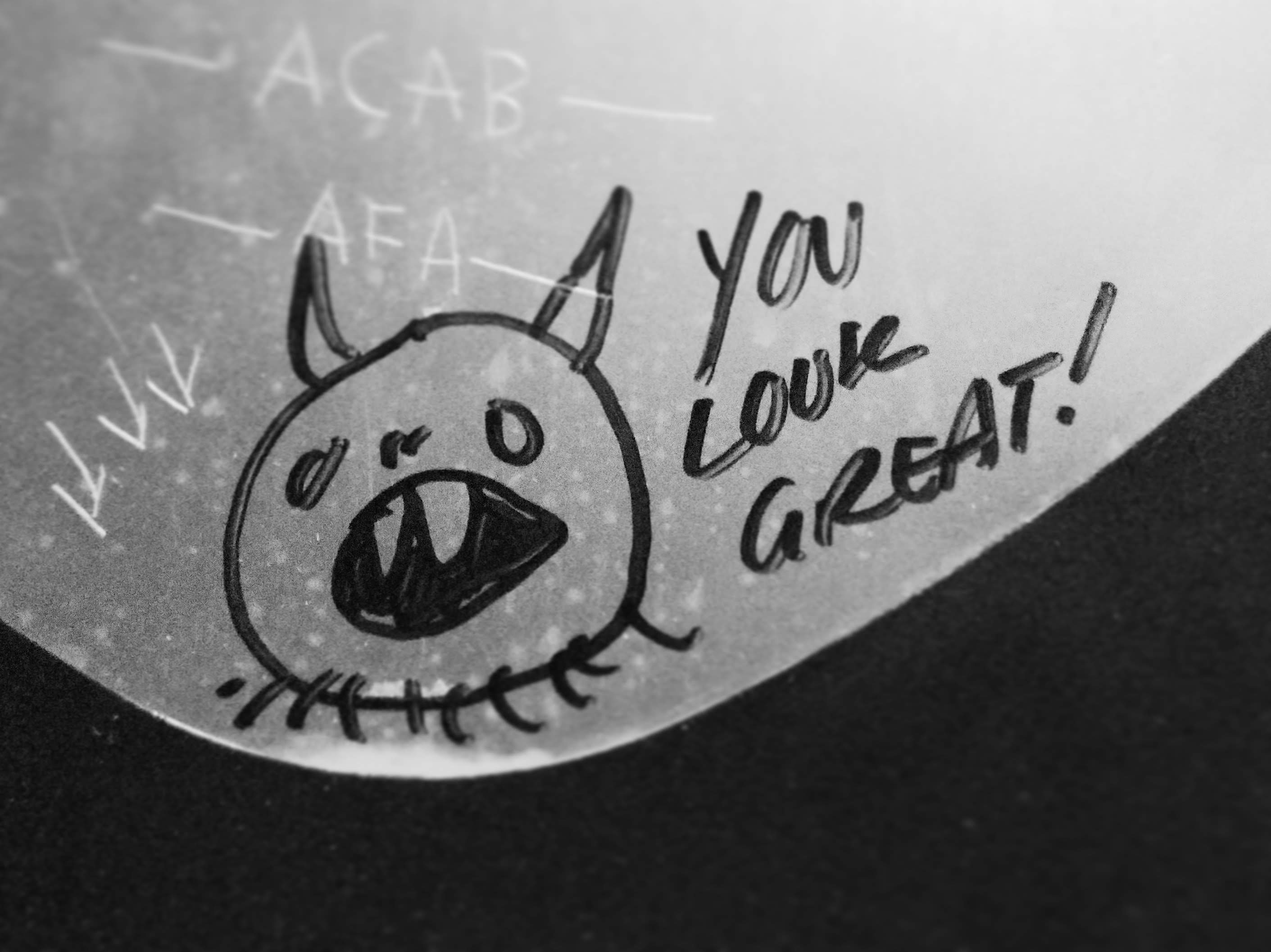 Graffiti in a bathroom stall: a monster next to text in all caps that says "You look great!"