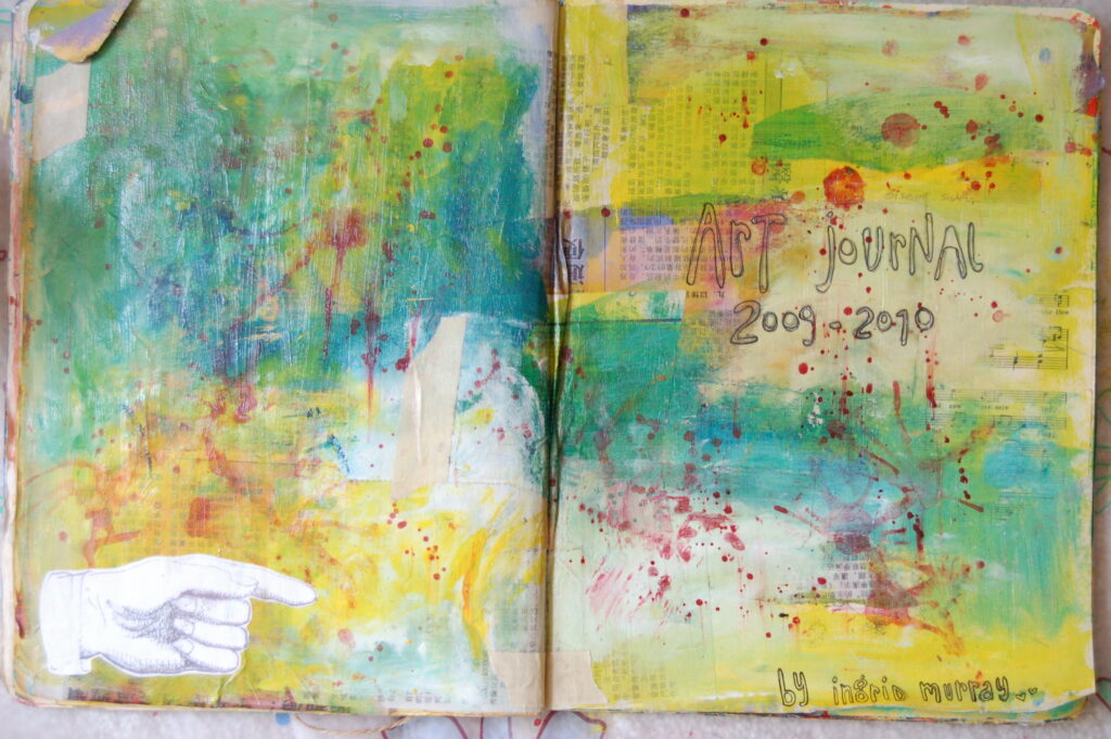 My first art journal opened fully to view a green, blue, and yellow cover. There is red splattered accents, a hand-drawn hand pointing, and in ballpoint pen: "Art Journal, 2009-2010, by Ingrid Murray."