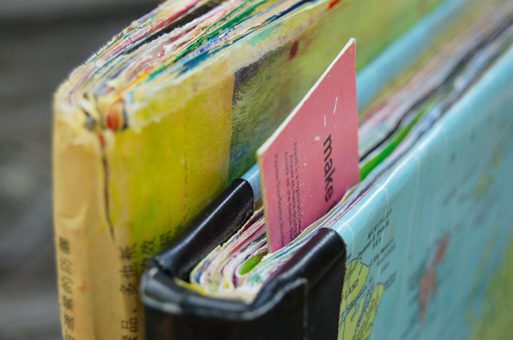 A close-up photo of two art journals, one yellow and the other blue. They are standing next to one another, with the spines close to the view. You can see the edges of colorful painted pages.