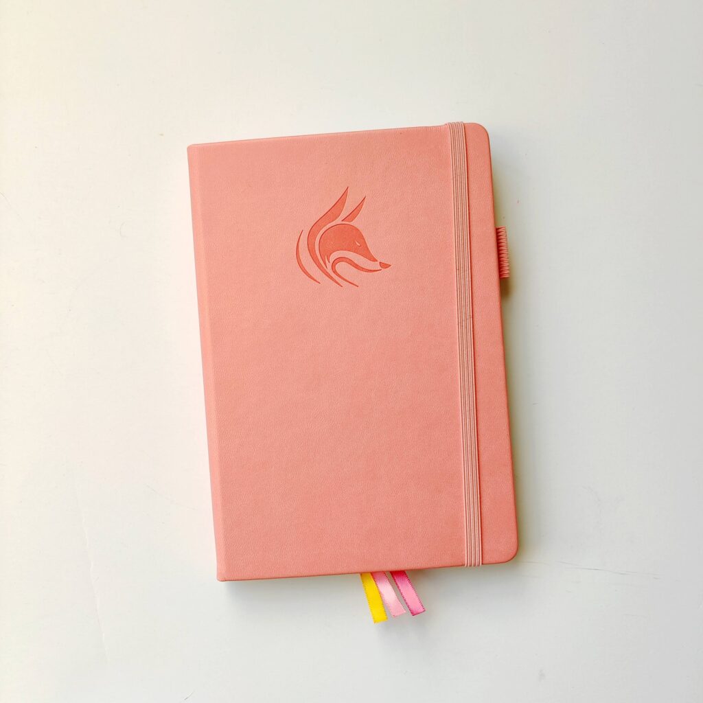 A salmon pink Clever Fox planner with a fox logo on the cover.