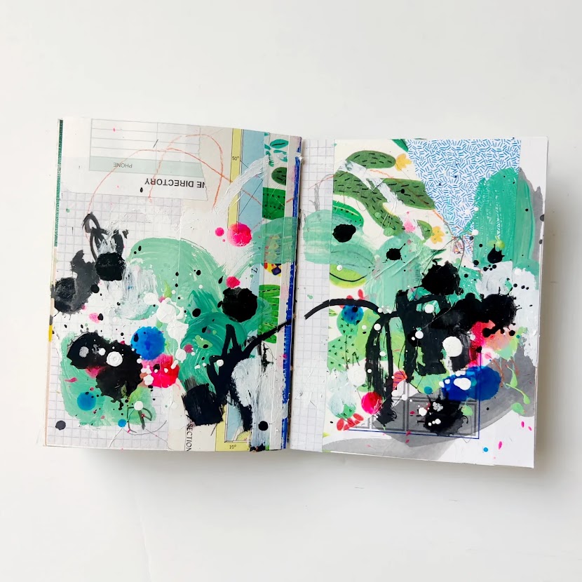 An open mixed media art journal. The pages are covered in a layer of collage, and on top of that are energetic marks in turquoise, black, blue, white, and hot pink. Much of the background peeks through.