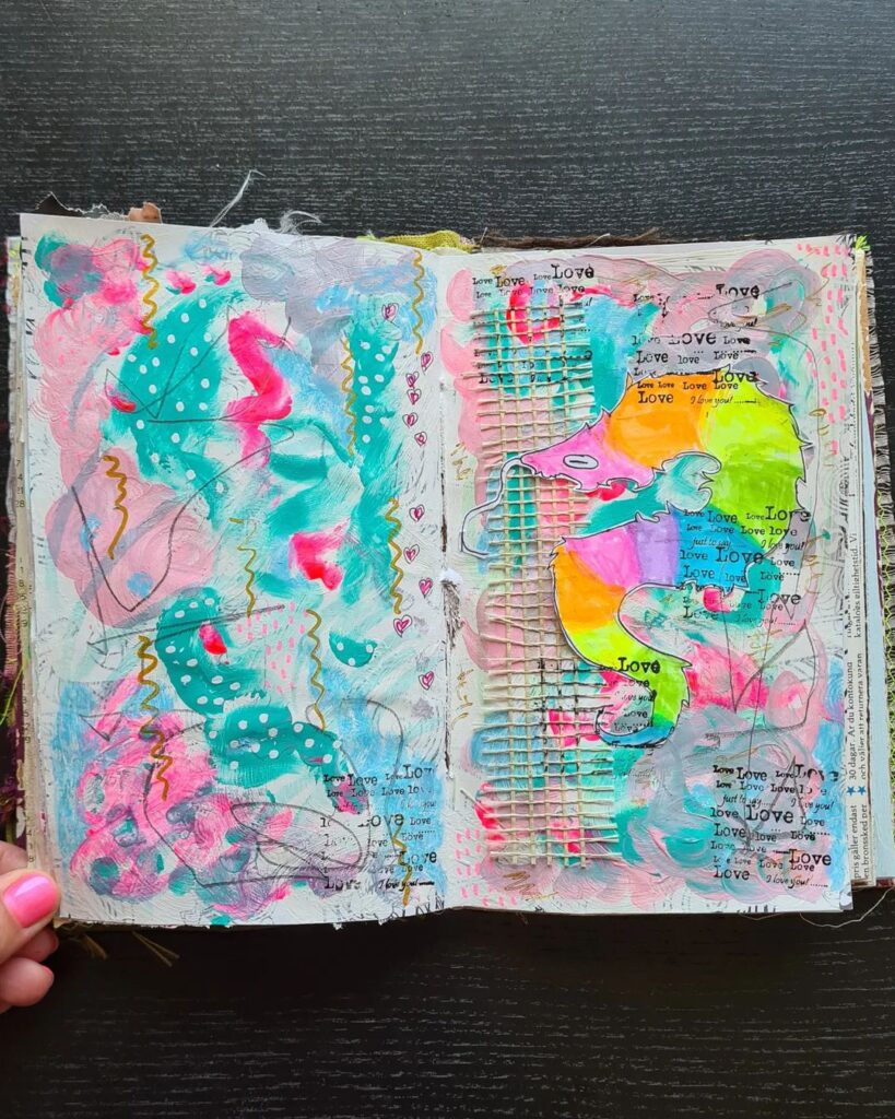 An open mixed media art journal with bright colors: neon pink and yellow, and teal.