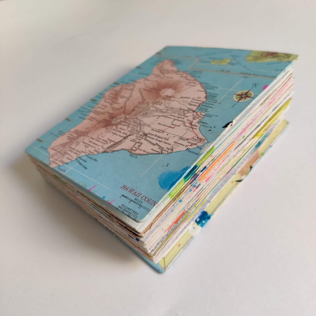 An art journal lying flat on a white background. The cover is an atlas page of one of the Hawaiian islands; the edges of colorful pages are visible.